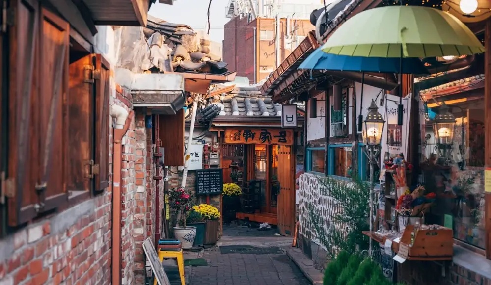 A perspective view of an aesthetic cafe in Ikseondong, blending a traditional Korean Hanok mud wall with modern glass windows and interior decorations.