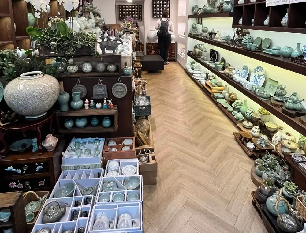 The interior of a traditional Korean pottery shop in Insadong, Seoul, showcasing elegant green celadon vases, tea sets, and various ceramic crafts on shelves.