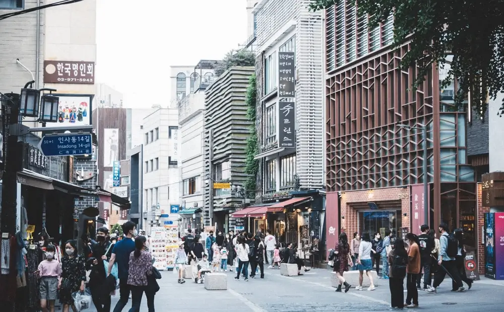 A busy and lively street view of Insadong cultural district in Seoul, showing tourists walking past traditional Korean shops and restaurants.