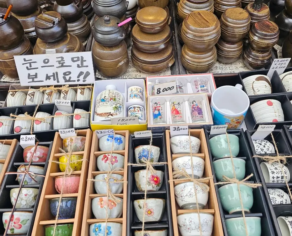 A display of traditional Korean souvenirs, ceramic tea cups with floral patterns, and small pottery items at a shop in Insadong, Seoul.