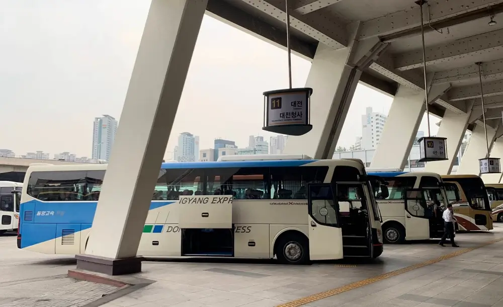 Korean express buses parked at a terminal boarding gate with a sign showing destinations