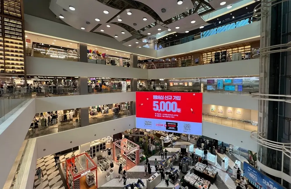 Modern multi-story interior of NC Department Store in Seoul, South Korea featuring shopping brands and a massive digital signage screen.