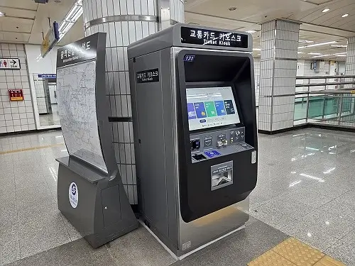 A grey automated ticket kiosk for purchasing and topping up transportation cards inside a Seoul subway station